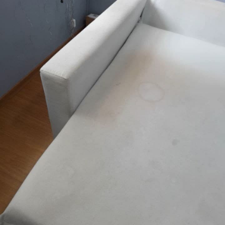 Assento de um sofá de canto branco com manchas circulares e área amarelada pelo uso